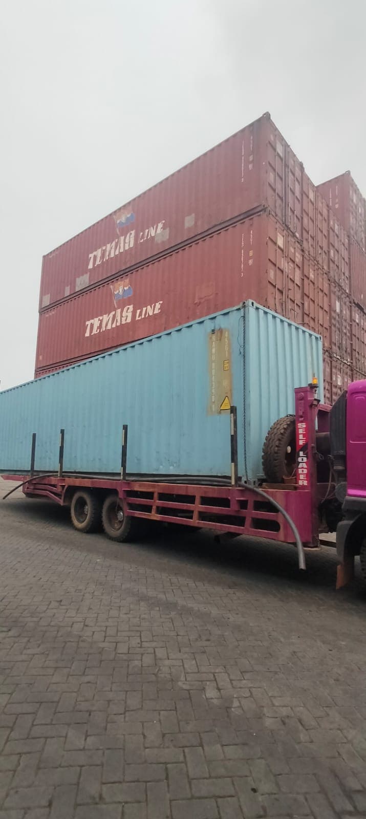 Truk self loader membawa kontainer biru muda di area penumpukan kontainer